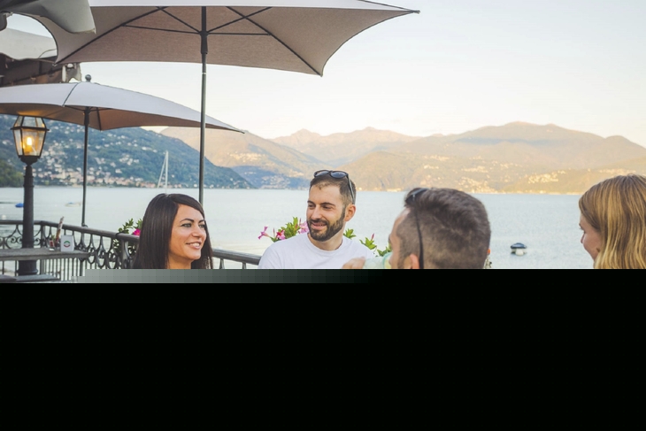Gruppe von Freunden beim Aperitivo am Seeufer bei Sonnenschein.