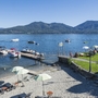 Strand am Lago Maggiore mit Sonnenschirmen und Booten auf dem Wasser.