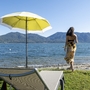 Frau am Ufer des Lago Maggiore mit gelbem Sonnenschirm.
