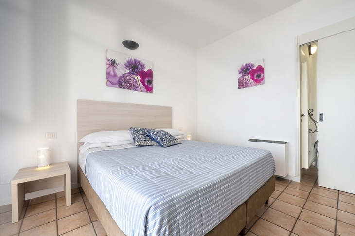 Zimmer mit Doppelbett, weißen Wänden, zwei Bildern und Fliesenboden.