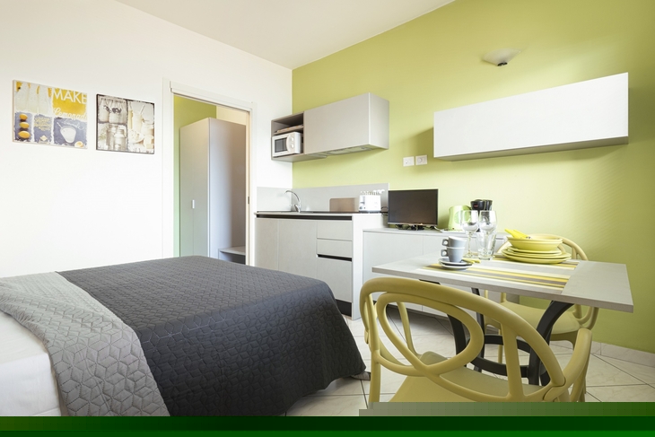 Helles Apartmentzimmer mit Esstisch, Bett und Küchenzeile.