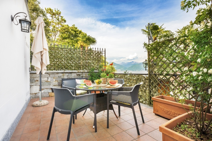 Terrasse mit Tisch, Stühlen und Melonenstücken, Ausblick auf See und Berge im Hintergrund.