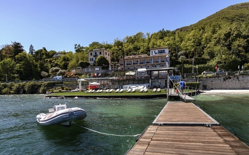 Steg führt zu einem Haus am See mit Boot im Wasser und Wald im Hintergrund.