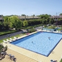 Großer Swimmingpool in einer Ferienanlage, umgeben von Liegestühlen und Bäumen.