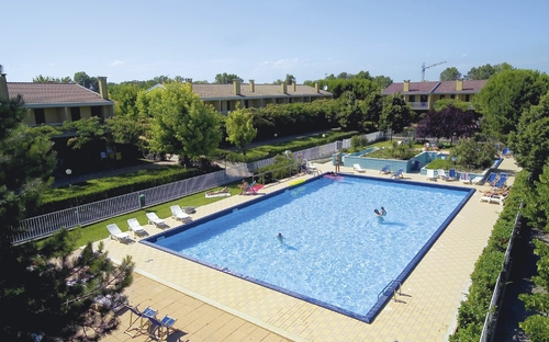 Großer Swimmingpool in einer Ferienanlage, umgeben von Liegestühlen und Bäumen.