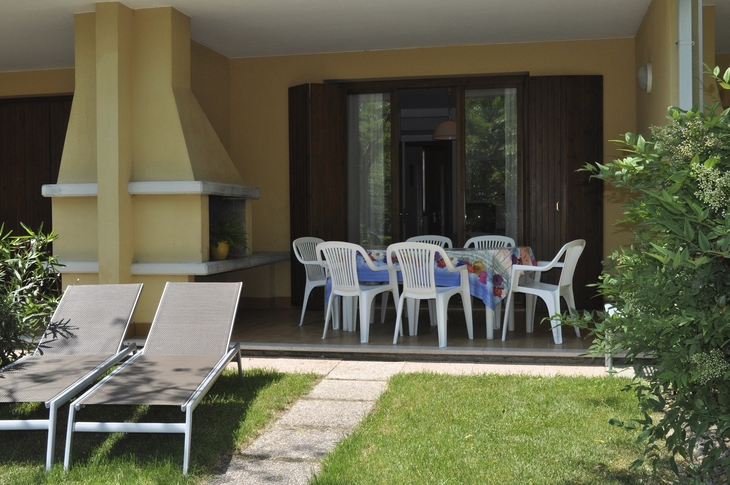 Terrasse mit Esstisch und Plastikstühlen eines Ferienhauses im Grünen.