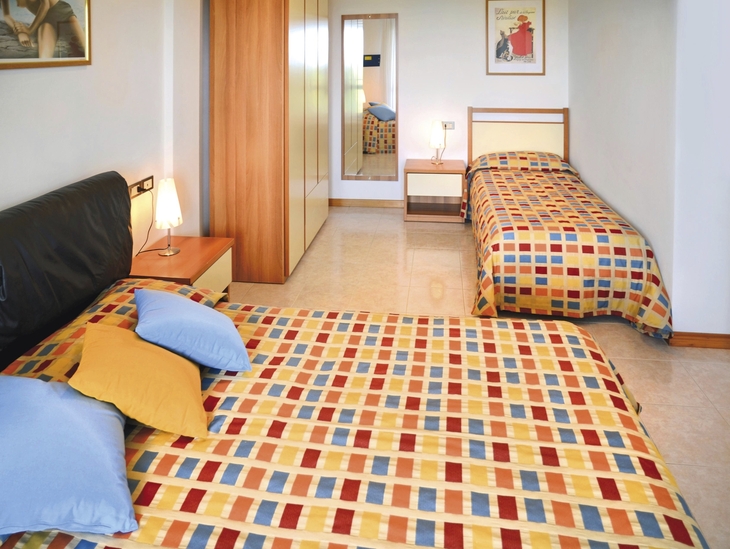 Hotelzimmer mit zwei Betten und bunter Bettwäsche.