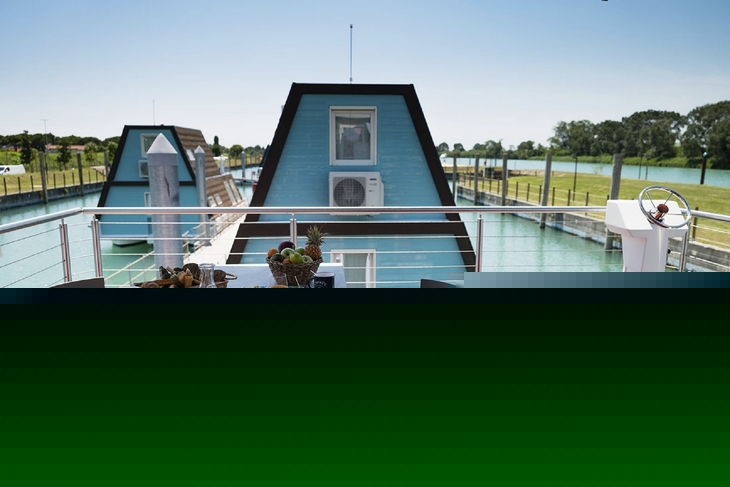 Terrasse mit Tisch, Stühlen, Frühstück und Blick auf schwimmende Häuser und Kanal.