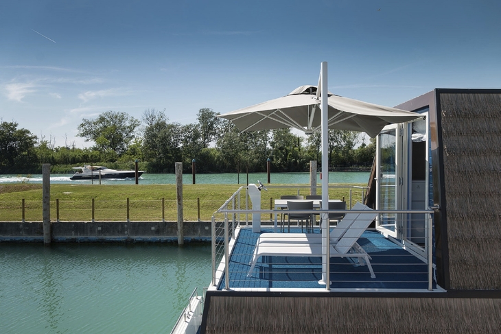 Terrasse mit Liegestühlen und Sonnenschirm an einer ruhigen Wasserlandschaft.