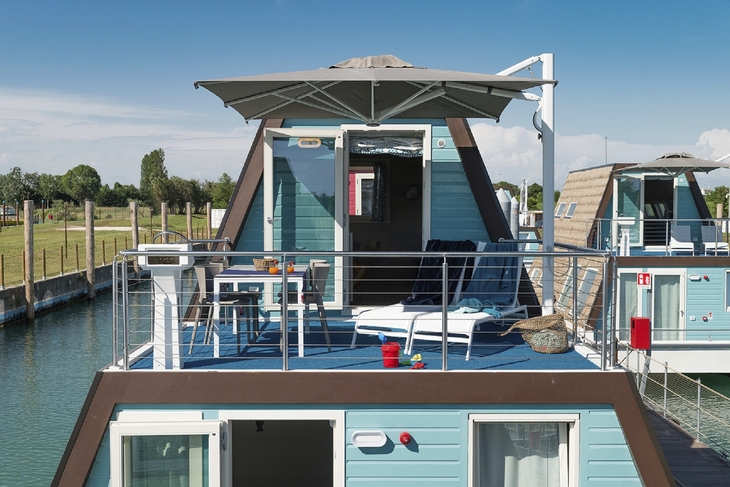 Hausboot mit Terrasse und Liegestühlen im Marina Azzurra Resort, blauer Himmel.