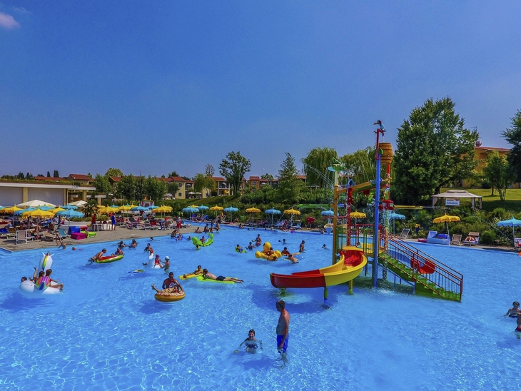 Personen im Freibad mit Rutschen und Poolspielzeug an einem sonnigen Tag.
