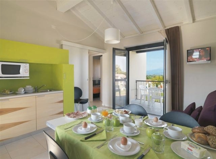 Essbereich in Ferienwohnung mit gedecktem Frühstückstisch, Küchenecke und Balkonblick.