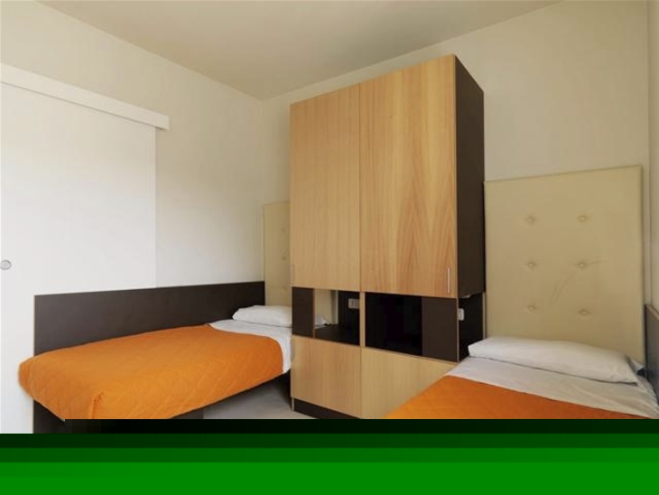 Zwei Betten mit orangefarbenen Decken und Wandschrank in einem Zimmer.