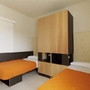 Zwei Betten mit orangefarbenen Decken und Wandschrank in einem Zimmer.