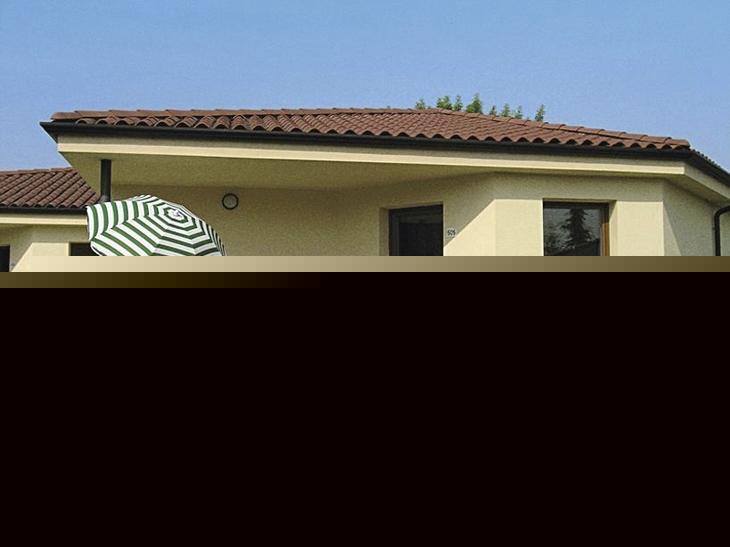 Bungalow mit Terrasse, Tisch, Stühlen und Sonnenschirm, umgeben von blühenden Rosen.