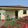 Bungalow mit Terrasse, Tisch, Stühlen und Sonnenschirm, umgeben von blühenden Rosen.