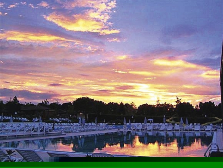 Sonnenuntergang über einem Wasserpark mit leeren Liegestühlen und Pool.