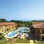 Ferienanlage mit Pool und Sonnenterrasse, Bäume im Hintergrund, sonniges Wetter.