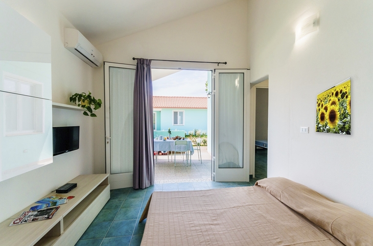Innenraum eines hellen Schlafzimmers mit Zugang zur Terrasse und Sonnenblumenbild an der Wand.