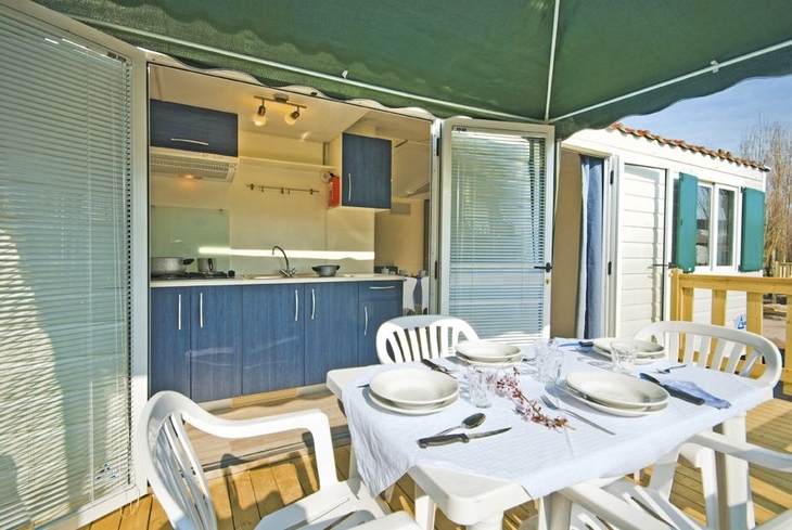 Terrasse eines Mobilheims mit gedecktem Tisch und geöffneter Küchentür.