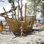 Kinder spielen auf einem Spielplatz mit Holzschiff in Ufernähe.