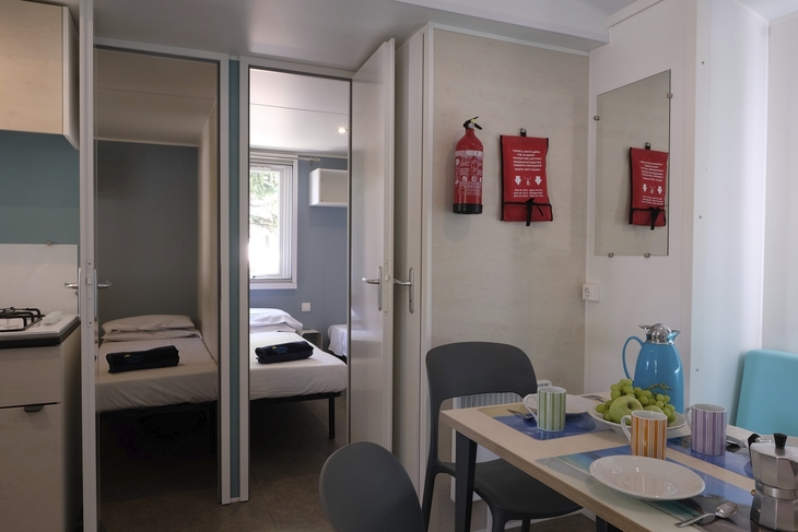 Innenansicht eines Mobilheims mit gedecktem Esstisch und einem Schlafzimmer im Hintergrund.