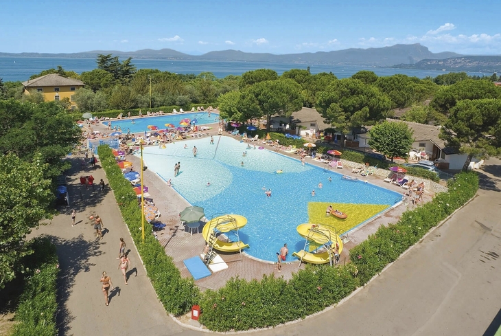 Luftaufnahme von Pools und Rutschen im Campingplatz mit Blick auf einen See und Berge.