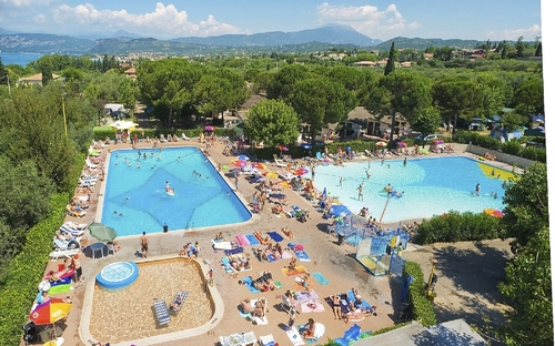 Luftaufnahme von zwei Pools und vielen Menschen auf einem Campingplatz bei Sonnenschein.