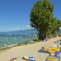Strand am Gardasee mit Menschen beim Entspannen und Baden unter blauem Himmel.