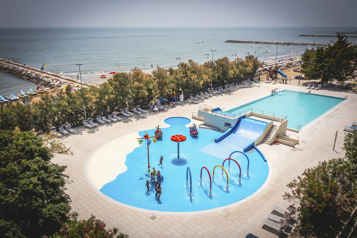 Blick auf Poolanlage und Meer im Ferienresort mit Rutschen und Spielbereich.