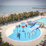 Blick auf Poolanlage und Meer im Ferienresort mit Rutschen und Spielbereich.