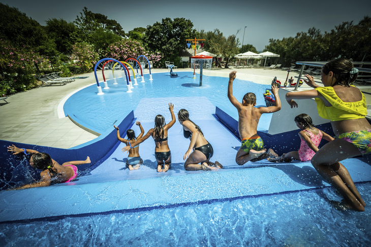 Kinder spielen auf einer Wasserrutsche in einem Pool unter freiem Himmel.