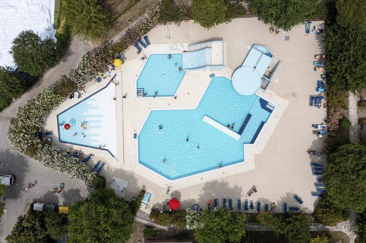 Luftaufnahme eines großen Pools mit Sonnenliegen und Bäumen im Happy Camp San Francesco.