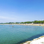 Strand mit Badegästen am Meer bei sonnigem Wetter, grüner Hintergrund.