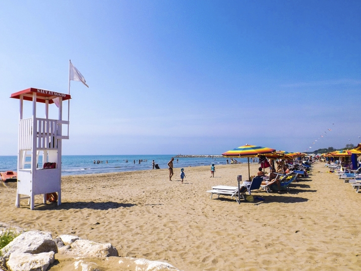 Sandstrand mit Sonnenschirmen, Liegestühlen und einem Rettungsturm am Meer.