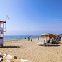 Sandstrand mit Sonnenschirmen, Liegestühlen und einem Rettungsturm am Meer.