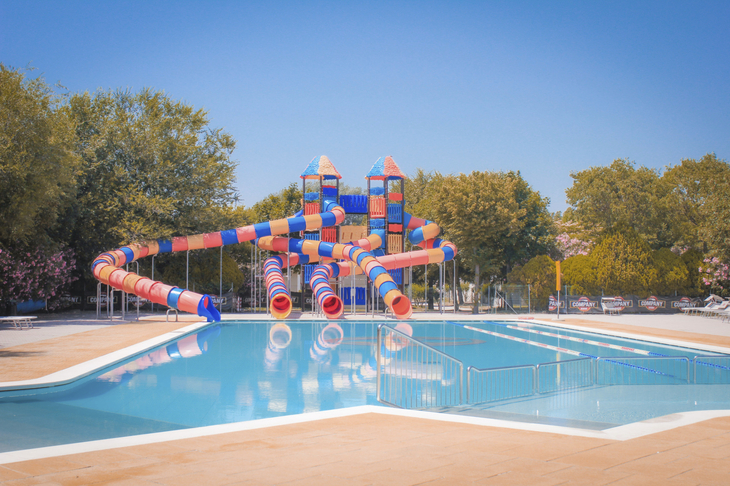 Pool mit bunten Wasserrutschen und Bäumen im Hintergrund.