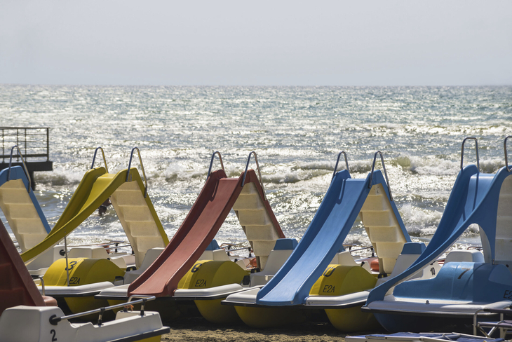 Tretboote mit Rutschen am Strand vor welligem Meer bei Sonnenschein