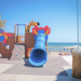 Spielplatz mit bunter Rutsche am Strand bei sonnigem Wetter.