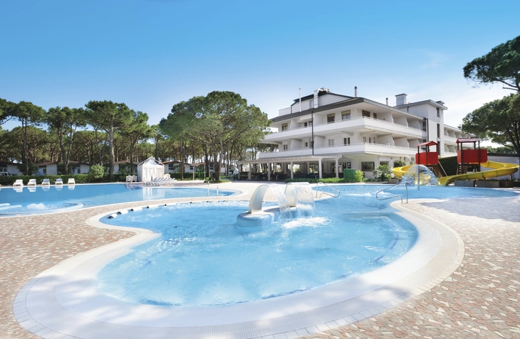 Poolanlage mit Rutschen und mehrstöckigem Gebäude im Hintergrund, umgeben von Bäumen.