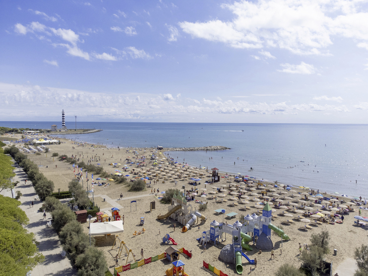 Strand mit Sonnenschirmen, Spielplatz und Leuchtturm im Hintergrund.
