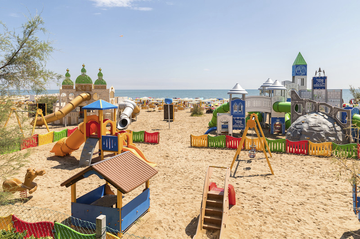 Spielplatz am Strand mit Rutsche und Klettergerüst, umgeben von bunten Zäunen.