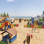 Spielplatz am Strand mit Rutsche und Klettergerüst, umgeben von bunten Zäunen.