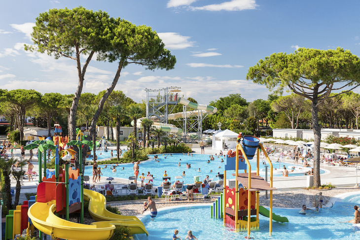 Wasserspielplatz mit Rutschen und badenden Menschen in einer Ferienanlage.
