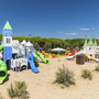 Spielplatz mit bunten Rutschen und Türmen auf Sand unter blauem Himmel.