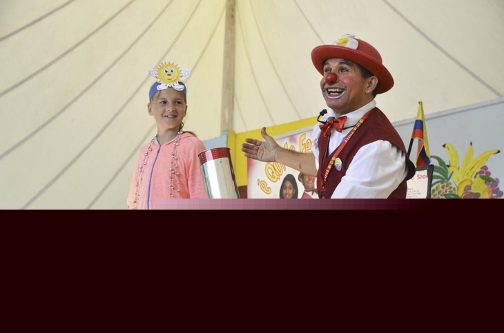 Clown mit roter Nase und Kind auf einer Bühne in einem Zelt.