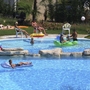 Menschen entspannen und spielen im Pool eines Campingplatzes mit Liegestühlen und Spielzeugen.