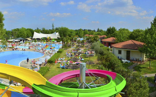 Feriendorf mit Pool, grüner Landschaft und bunter Rutsche auf Campingplatz.