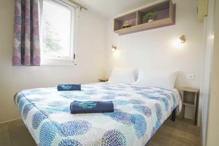 Schlafzimmer eines Mobilheims mit Doppelbett, bunten Vorhängen und modernem Dekor.