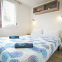 Schlafzimmer eines Mobilheims mit Doppelbett, bunten Vorhängen und modernem Dekor.